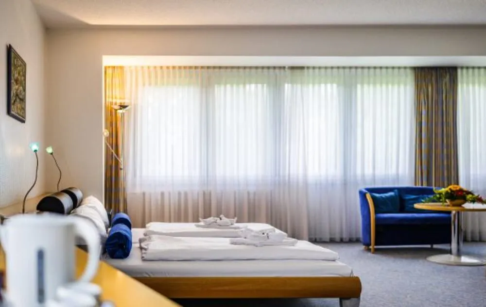 Helles Doppelzimmer im Seepark Hotel mit großen Fenstern, Sofa und Blick ins Grüne